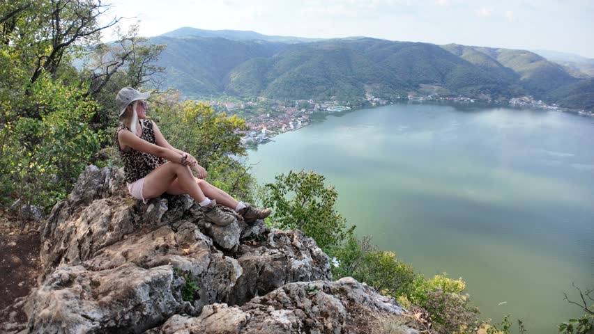 Woman traveler sitting on a rock admiring the stunning landscape of the Danube river gorge, offering a breathtaking view of the Iron Gates natural border between Serbia and Romania