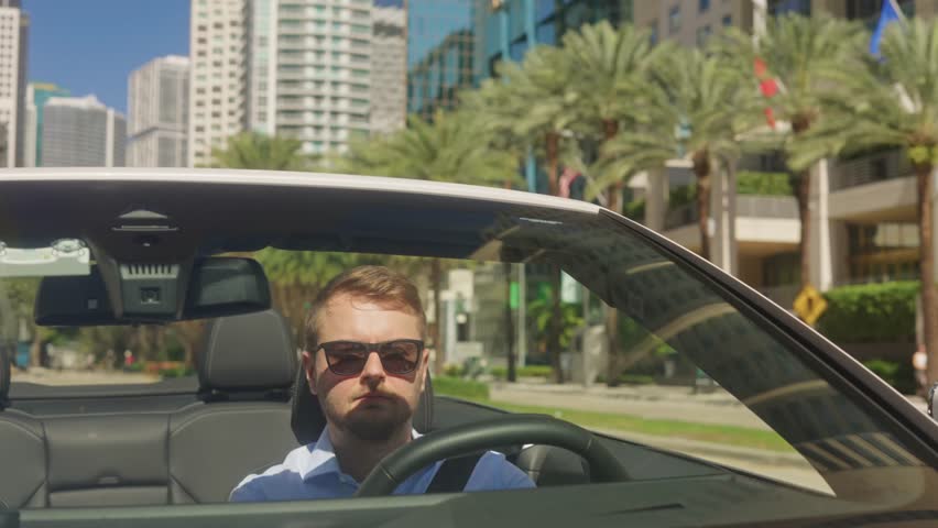 Front view of a tourist driving a white convertible in Miami, Florida, sunny streets, modern urban buildings, luxury lifestyle, travel, sightseeing, city adventure