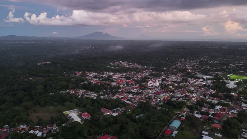 Experience beauty of colorful town nestled in lush greenery with mountains in background during sunset.