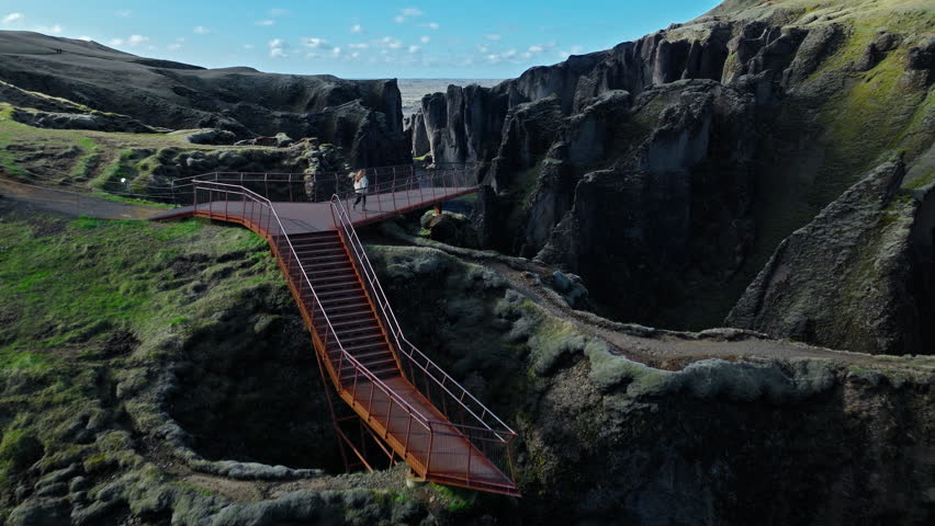 Tourist woman exploring viewing platform Fjadrargljufur canyon Iceland. 4K cinematic drone footage captures volcanic cliffs and turquoise river gorge.