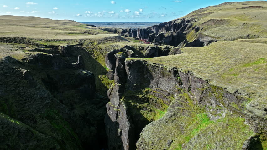 Aerial view of Fjadrargljufur canyon Iceland opening to coastline. 4K cinematic drone footage captures volcanic cliffs and winding river flowing to the ocean.