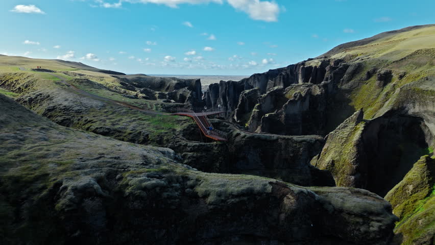 Drone aerial wide view of Fjadrargljufur canyon Iceland. 4K cinematic footage shows volcanic cliffs stretching across valley with river flowing below.