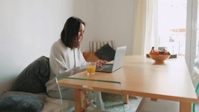 A young woman sits at her dining table, working remotely. She types on her laptop and enjoys a glass of orange juice. - Powered by Shutterstock - Get 15% off with code: PIKWIZARD15