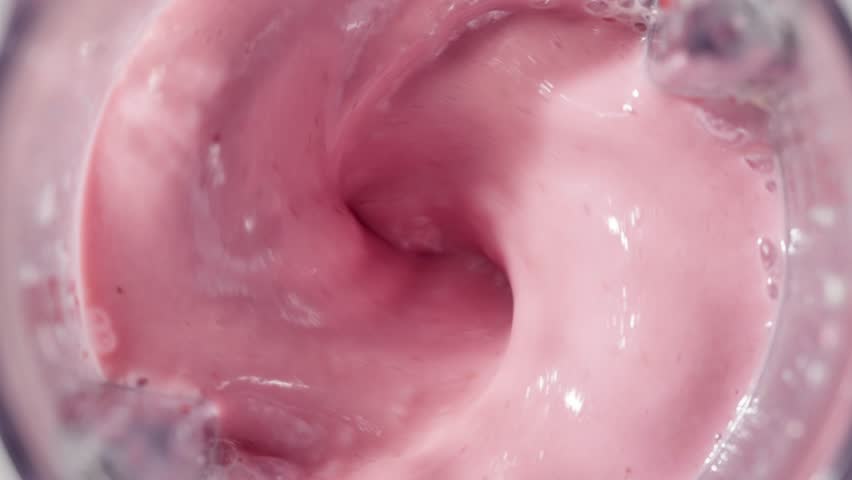 Strawberry and banana pink milkshake blended in blender with splashes. top view. slow motion. Healthy protein smoothie drink concept , food closeup. Protein powder falling in smoothie from spoon