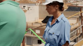 Female architect in white hard hat overseeing and conversing with male construction worker on rooftop, reviewing renovation plans with scaffolding in background  - Powered by Shutterstock - Get 15% off with code: PIKWIZARD15