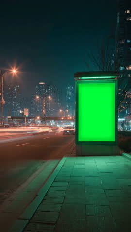 Outdoor blank green chroma key screen billboard at night in city street time lapse. Empty chromakey light box with copy space for advertisement mockup timelapse.