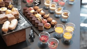 slow-motion video shows a dessert buffet table filled with assorted sweets, including layered chocolate cakes, colorful macarons, mini tarts, cream puffs, and elegant glass cups of mousse, panna cotta - Powered by Shutterstock - Get 15% off with code: PIKWIZARD15