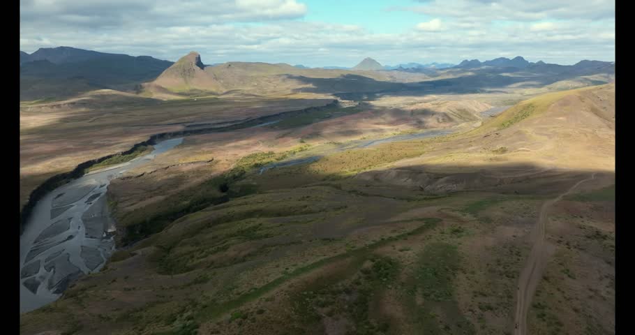 Scenic shot of a mountain landscape with high peaks, forest, river, and valley under cloudy sky, ideal for nature, travel, and adventure themes.