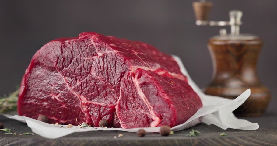 Fresh raw beef meat with pepper and thyme turning on dark wooden cutting board