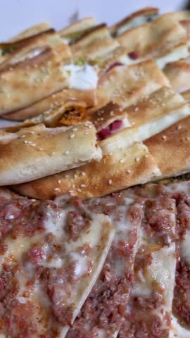 Vertical close-up of assorted Middle Eastern flatbreads topped with cheese, minced meat, herbs, and sesame seeds. Perfect for food reels, restaurant ads, bakery promos, and Mediterranean cuisine .