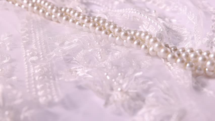 Sliding beautiful pearls along lace fabric on white background, closeup