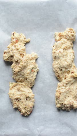 overhead view of savory biscotti dough being shaped on a parchment lined baking sheet, top view of savory cookie dough on parchment paper