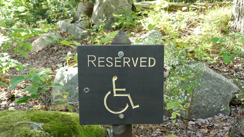 Handicapped parking reserved sign in nature park with moss cover rocks in background
