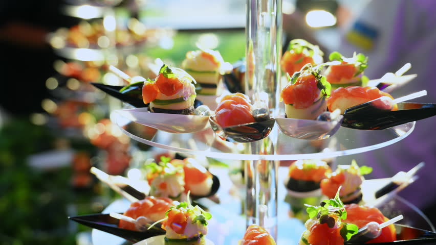 Arranged sushi platter served on elegant multi-tiered display stand. Vibrant pink and orange tones of fresh salmon and tuna contrast with the black serving spoons