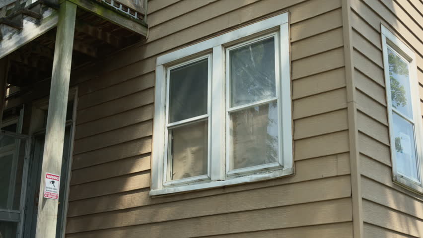 Close-up of an old residential building exterior with worn wooden siding and aged windows. Peeling paint and weathered frames highlight the need for renovation or repair