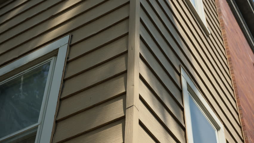 Close-up of old residential building exterior, corner of house with worn wooden siding and aged windows. Peeling paint and weathered frames highlight the need for renovation