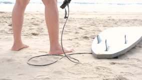 A surfboard fastened to a man's feet on the beach in the sand, close-up view from behind. - Powered by Shutterstock - Get 15% off with code: PIKWIZARD15