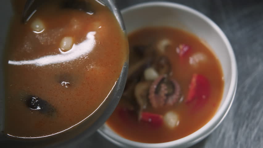 Preparing asian soup. Pouring meal. Chef hand serving hot dish of octopus shrimp squid mushrooms. Liquid spicy tomato broth ladling to bowl.