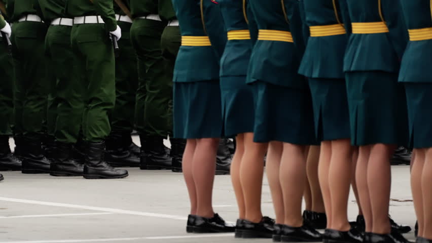 Rows of uniformed personnel standing in strict formation on a parade ground, showcasing green attire, polished black footwear, synchronized stance, and ceremonial discipline.