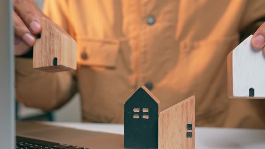 With hands on the laptop and wooden houses in front, highlights the pursuit of sustainable land utilization, efficient resource management, and community-focused design in the real estate sector.
