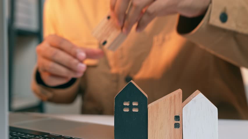A real estate developer arranges wooden houses while working on a laptop, symbolizing sustainable land use, urban innovation, and the integration of technology in modern property development.
