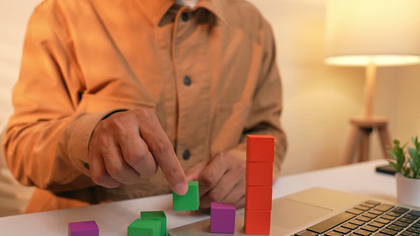 A businessman arranges colored blocks into stacked layers, symbolizing data organization, resource allocation, growth planning, decision-making processes and the structured pursuit of long-term goals.