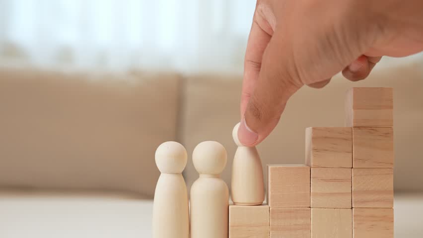 A hand moves a wooden child figure up block steps to the top, beside parent figures, representing growth, encouragement, achievement, parental support, guidance, aspiration, and family success.
