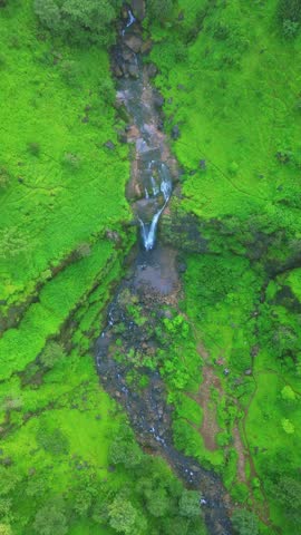 An aerial top view of Bahuli Falls, Maharashtra, showcases a stunning waterfall cascading through dense green forest and rocky hills, surrounded by untouched nature 4K