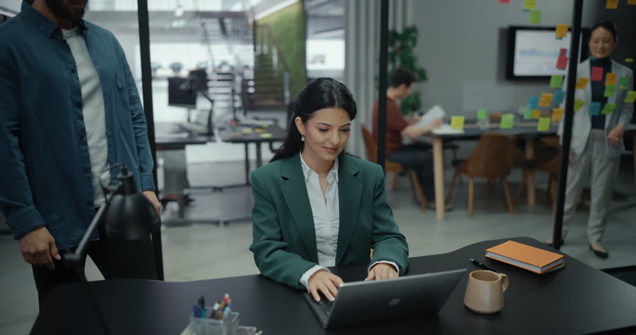 Young Female and Male Specialists Having a Conversation in Office, Looking at a Laptop Computer, Discussing Financial Reports and Business Data for a Company Project