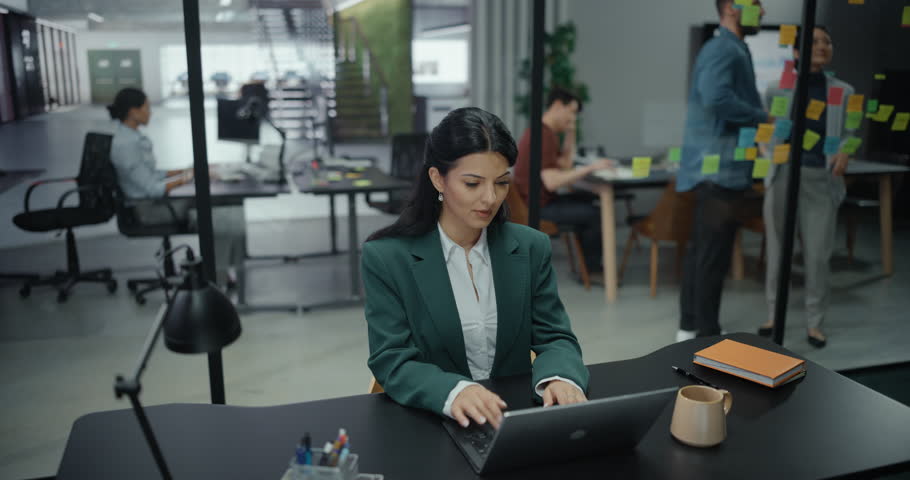 Beautiful Manager Working on Laptop Computer in Big Business Office with Diverse Colleagues in the Background. Businesswoman Preparing for a Marketing Plan Meeting Discussion with Board Members