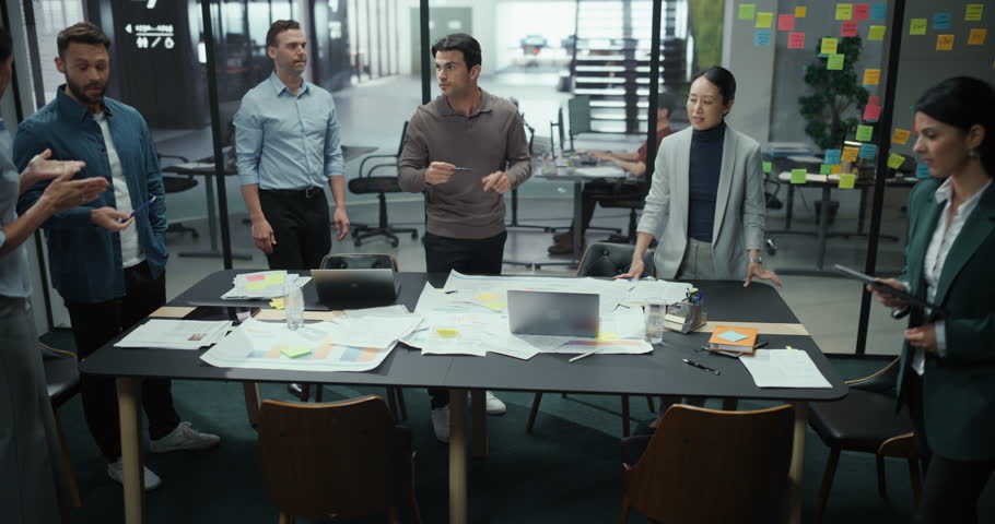 Specialists Working in a Modern Office, Utilizing Laptop Computers and Paper Documents for the Meeting. Men and Women Standing, Hands on Table, Collaborating on a Project and Exchanging Information