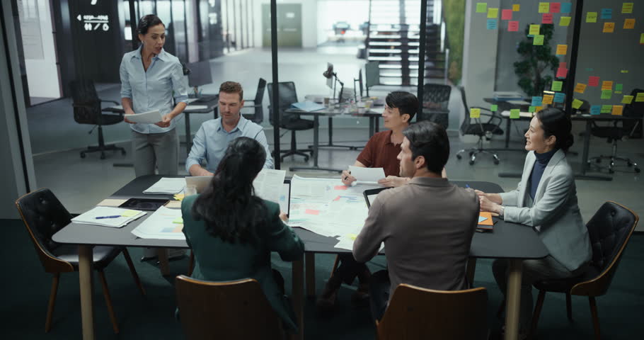 Diverse Team of Business Professionals Attending a Corporate Presentation in a Modern Conference Room. Female Manager Stands in Front, Delivering a Keynote While Colleagues Listen and Take Notes