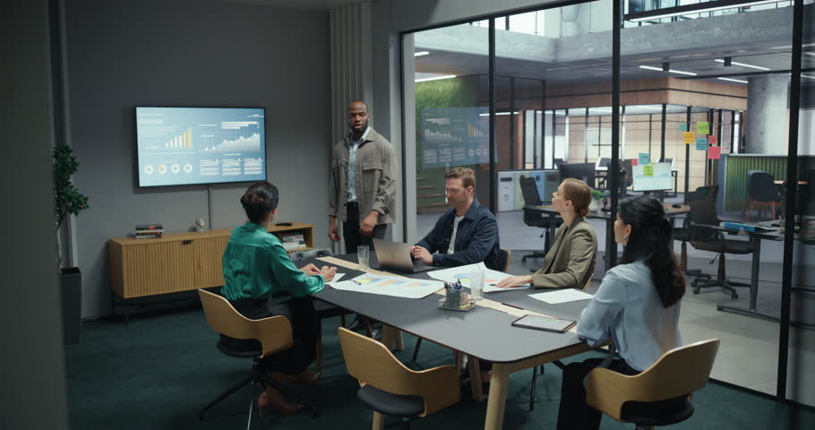 Diverse Team of Business Professionals Attending a Corporate Presentation in a Modern Conference Room. African Manager Stands in Front, Delivering a Keynote While Colleagues Listen and Take Notes