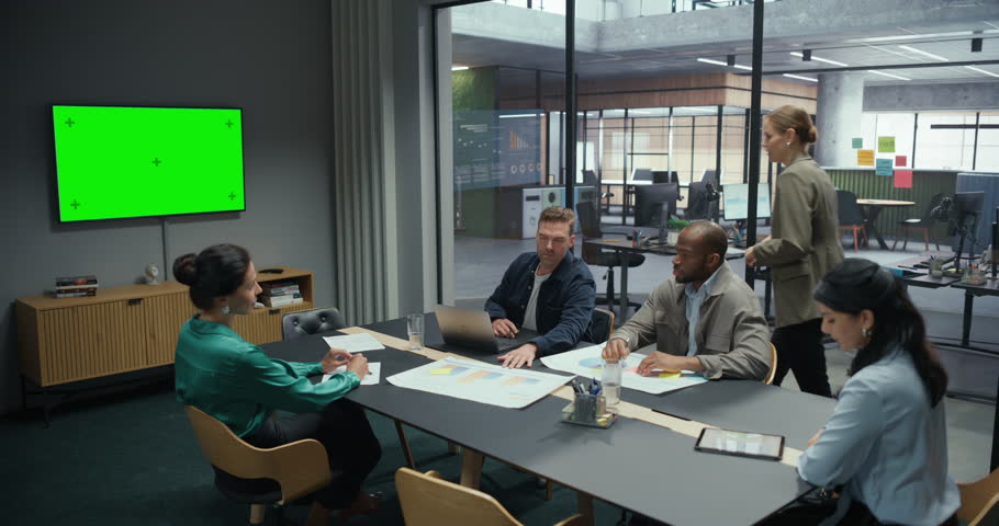 Female Manager Stands at the Front of a Conference Room, Delivering a Presentation with Green Mock Up Template on Screen. Colleagues Sit Around the Table, Listening and Taking Notes