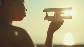 Happy childhood, little boy holding wooden aircraft model in hands and playing. Back view against bright sun in sky, sunset or sunrise above sea or ocean, cinematic slow motion, children game outdoors - Powered by Shutterstock - Get 15% off with code: PIKWIZARD15