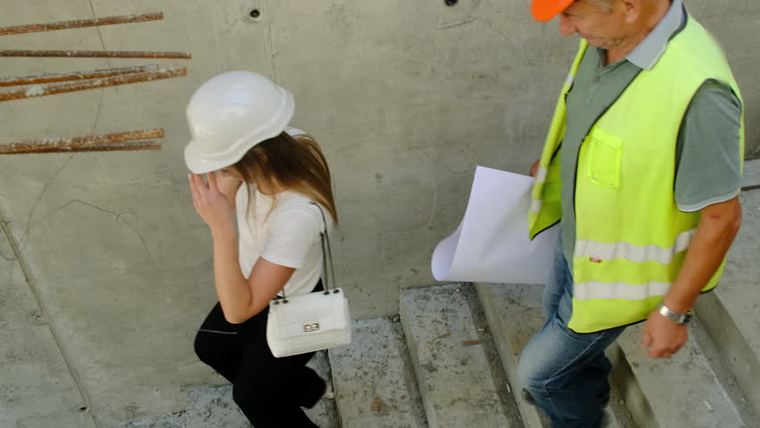 Lady expert and builder walk down steps of building. Specialists in hard hats inspect site during construction work visiting special areas