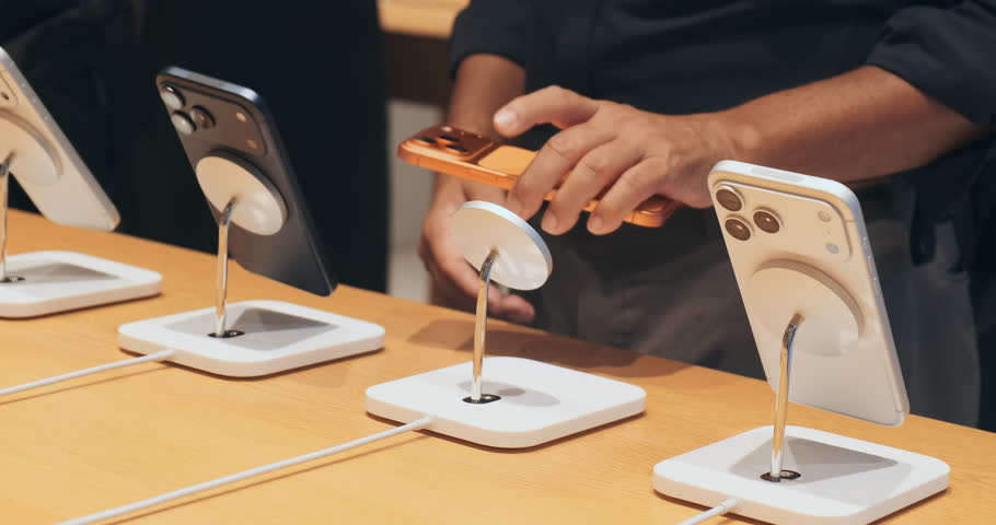 Customer compares new Phone models at Store. Man choosing smartphone in electronics showroom indoor. Hands on testing features at retail demo table. Modern consumerism tech shopping interior