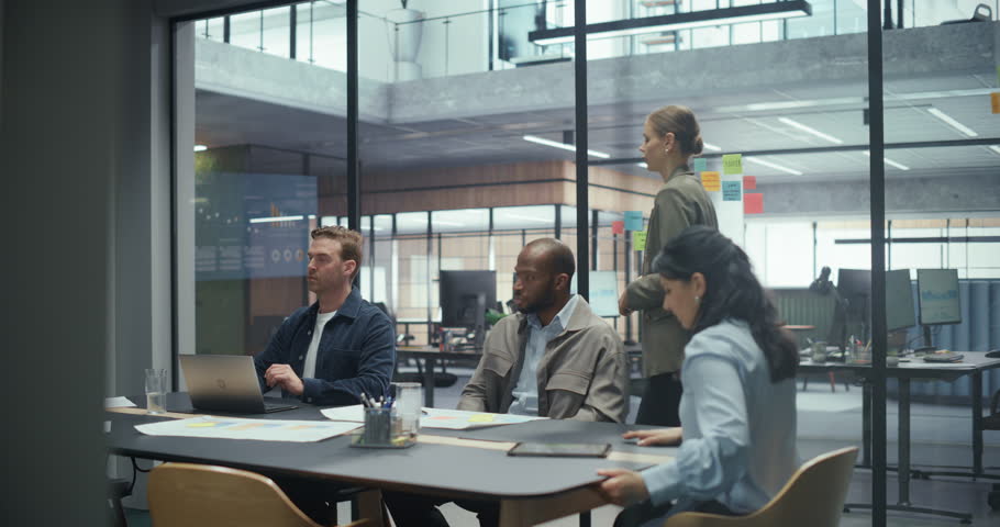 In Modern Office: Female Project Manager Presents New Business Plans to a Group of Diverse Professionals. Team Pays Attention to Her Speech while Reviewing Slides Projected Behind Her