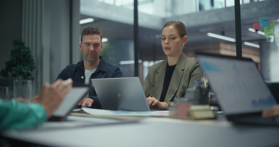 Employees Sitting Side by Side in a Conference Room, Working Independently on Laptops. Male and Female Having a Conversation. Group is Busy with Reports and Project Planning