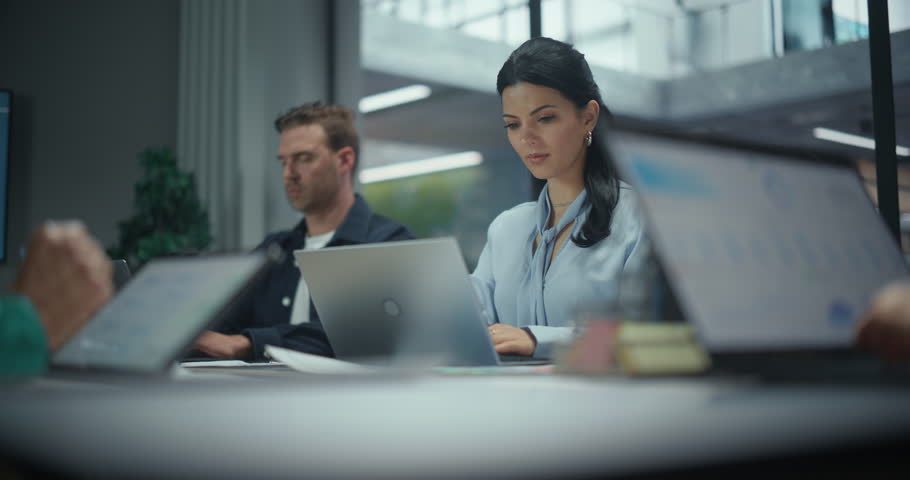 Portrait with a Female Seated Together with Office Workers Behind a Large Table, Each Working on Laptop Computers During a Team Session. Colleagues Concentrating on Corporate Tasks