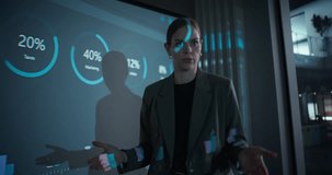 In a Dark Office Space, Female Manager Stands at the Front of the Room Delivering a Corporate Presentation. She Outlines Project Objectives to the Team while Data and Visuals Appear on Screen - Powered by Shutterstock - Get 15% off with code: PIKWIZARD15