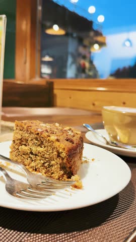 4K Vertical shot of Cappuccino and fresh Carrot cake on cafe table during evening at Manali, Himachal Pradesh, India. Tourist enjoying food in authentic restaurant. Coffee on table.