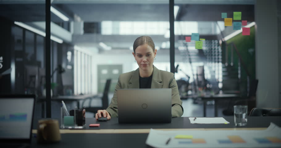 Successful Caucasian Woman Sitting Behind a Desk and Working on a Laptop Computer in an Office Environment. Female Feeling Positive while Working on a Profitable Financial Project