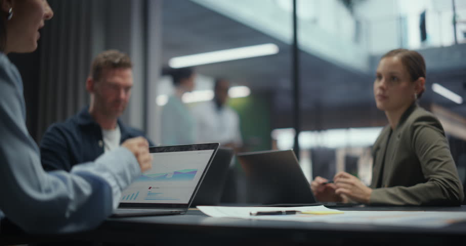 Businesspeople Sitting Around a Conference Table with Colleagues, Discussing Projects and Using Laptop Computers. Employees Research and Collaborate in a Modern Office. Slow Motion Footage