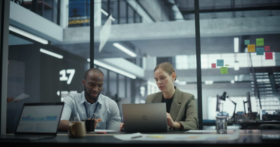 Diverse Couple of Professional Businesspeople Meeting in the Modern Office Conference Room. Creative Team Sitting Behind a Table, Working on Laptop, Discussing Corporate Strategy, Financial Reports