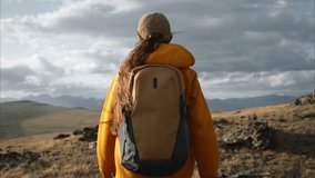 A close-up view of a female hiker with backpack and trekking poles climbing up a mountainside and raising her arms in triumph upon reaching the summit. Solo mountain travel - Powered by Shutterstock - Get 15% off with code: PIKWIZARD15