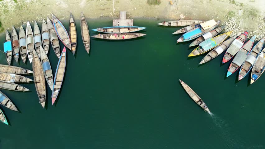 Aerial view of the boats docked along the riverbank, casting long shadows on the water, a tranquil scene of life near the river, Riverside, Rajshahi Division, Bangladesh.
