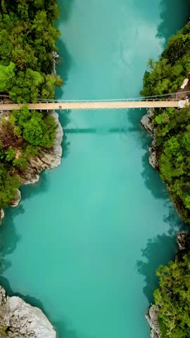 Aerial view of a turquoise river running under a bridge, surrounded by lush green trees, Kokatahi, West Coast Region, New Zealand.