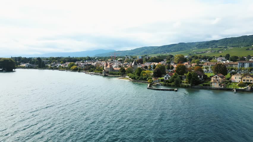 Aerial view of Rolle, nestled by Lake Geneva, presents a tranquil scene with the medieval castle and quaint houses against the backdrop of rolling hills, Rolle, Vaud, Switzerland.
