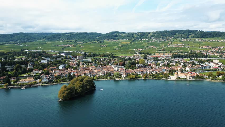Aerial view of Rolle, Switzerland, where terracotta rooftops meet the tranquil blue waters by the verdant Ile de la Harpe, Place des Tilleuls, Rolle, Vaud, Switzerland.